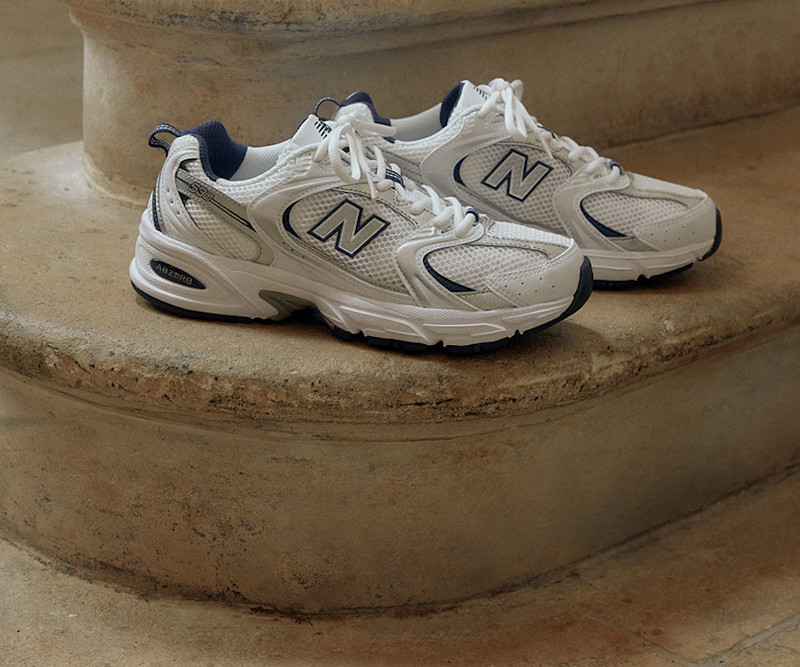 Et par hvite New Balance joggesko med mørkeblå detaljer står på en steintrapp.