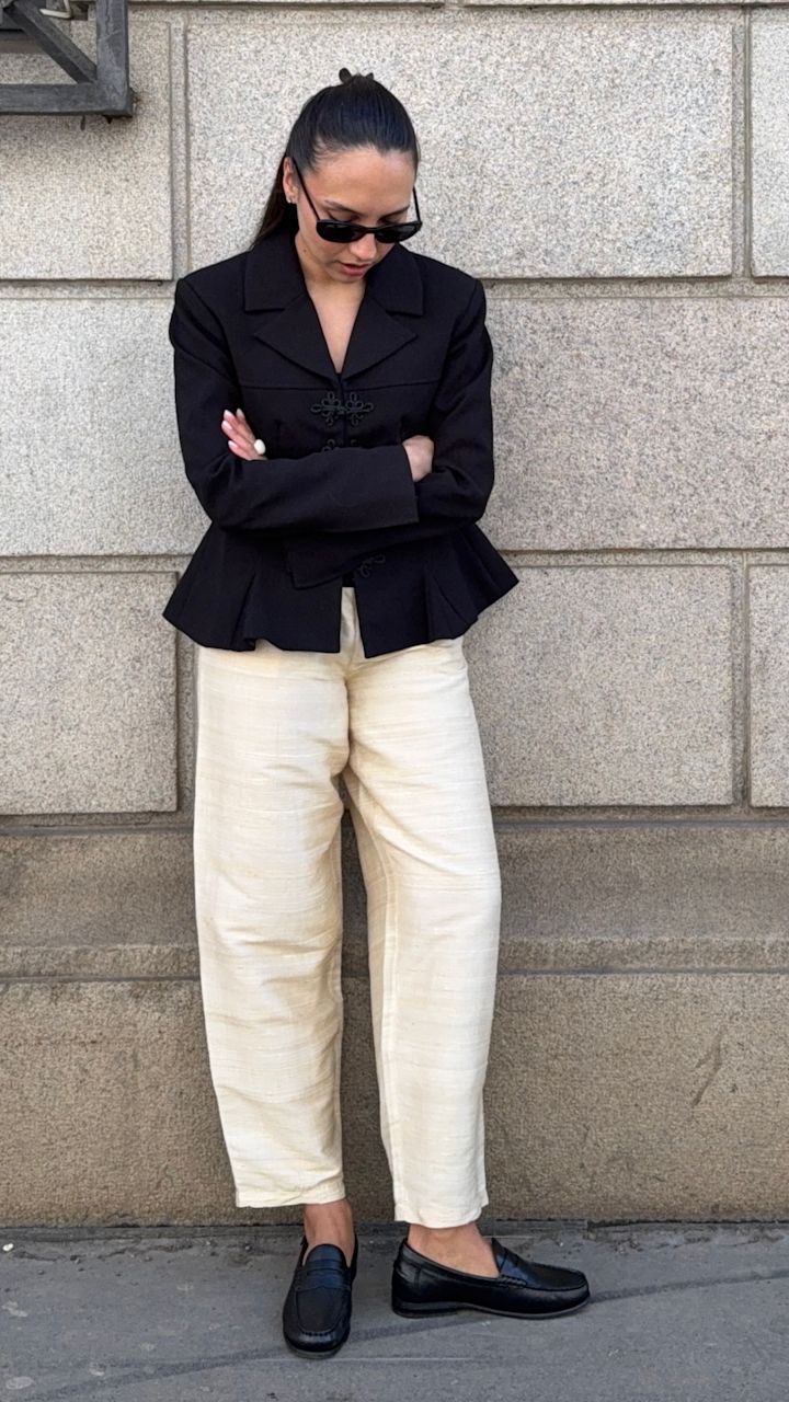 Influenser Ingrid Edvinsen i svart blazer og kremfargede bukser, med svarte klassiske loafers i skinn fra Stockholm Design Group mot en steinvegg.