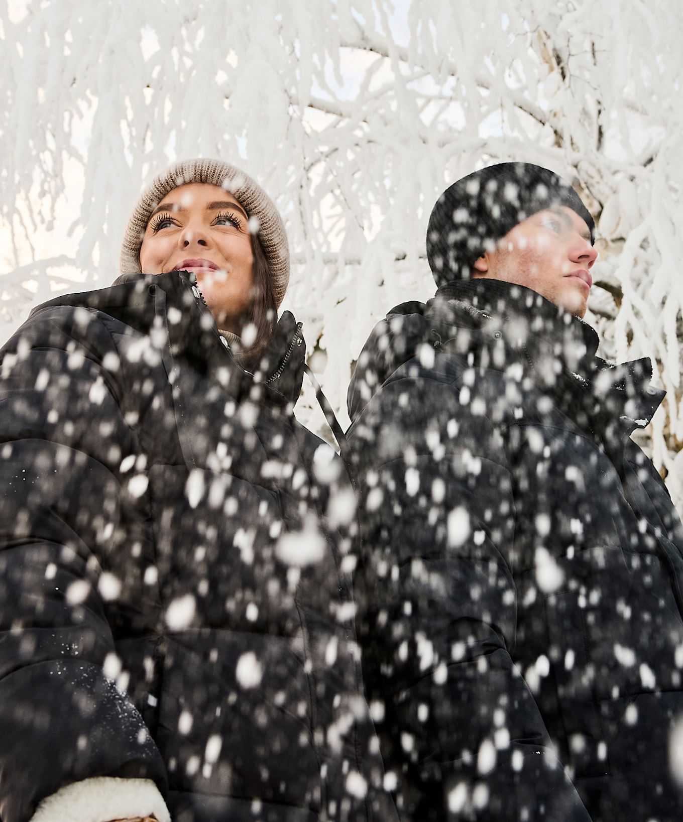 Två personer i svarta vinterjackor står i ett snöigt landskap med frostiga träd i bakgrunden.