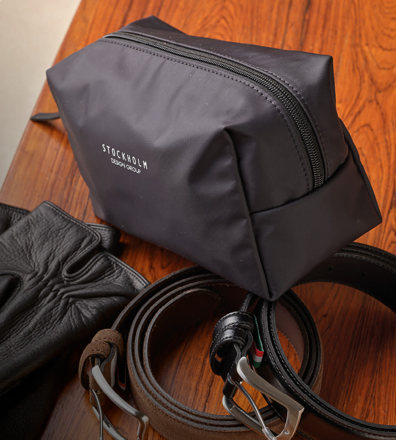 Svart necessär från Stockholm Design Group på träbord med svart och brun läderbälte i bakgrunden.