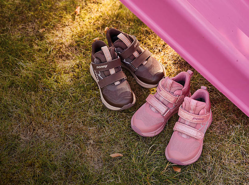 Två par höstskor från Ponny på gräs: bruna och rosa med kardborreband, sportig stil, vid en rosa rutschkana.