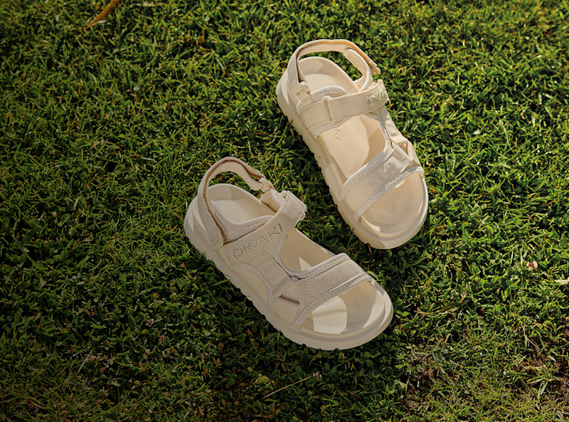 Beige sportsandaler med kardborreband och tjock sula ligger på grönt gräs. Casual sommarstil.