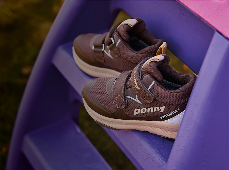 Bruna barnsneakers från Ponny med kardborreband och Sympatex-membran, placerade på lila trappsteg utomhus.