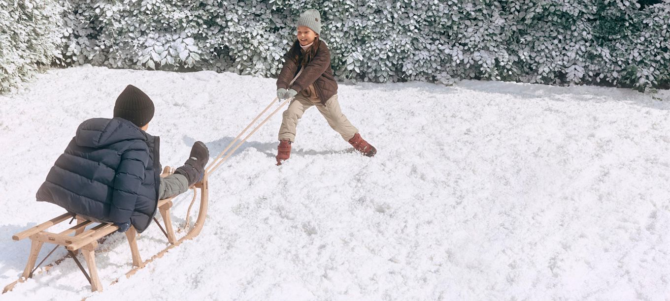 Barn leker i snön, en drar en träsläde. Personen som drar har röda vinterkängor, den på släden har Snow Mountain från Ecco.