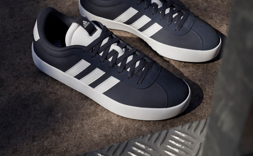Mørkeblå Adidas sneakers med hvite striper og såle, i sporty casual stil, plassert på grått underlag.