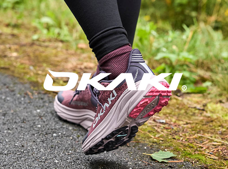 Okaki trail-løpesko i burgunder og rosa med grovt grep, brukt utendørs på sti omgitt av natur.