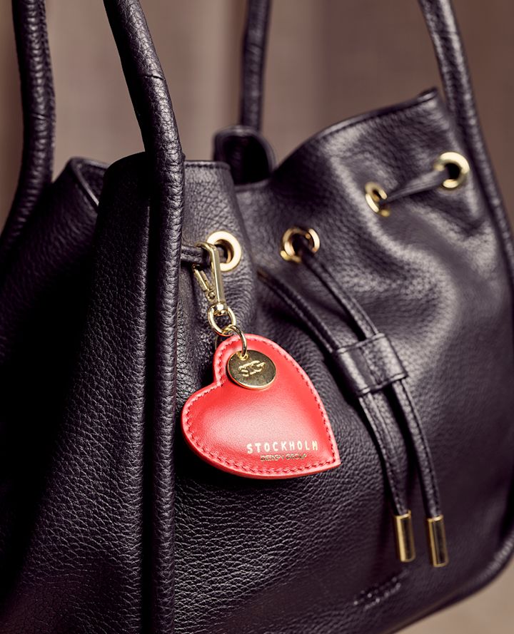 Svart skinnveske med gulldetaljer og en rød hjerteformet nøkkelring med "STOCKHOLM" skrevet på.