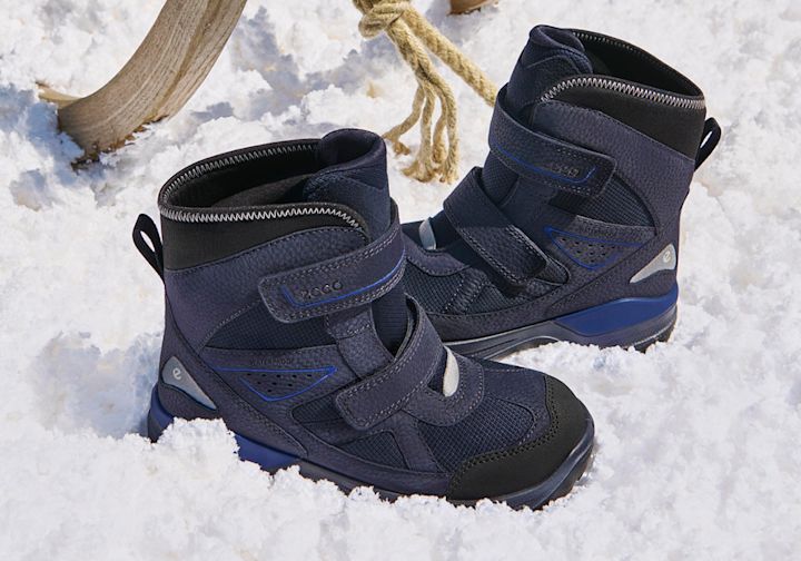 Mörkblå vattentäta vinterkängor för barn med kardborreband och blå detaljer, placerade i snö.