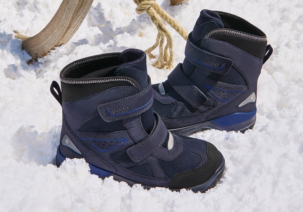 Mörkblå vattentäta vinterkängor för barn med kardborreband och blå detaljer, placerade i snö.