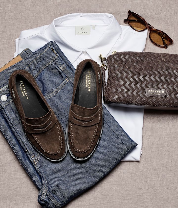 Mørkebrune semsket loafers fra Stockholm Design Group, stylet med blå jeans, hvit skjorte, brun veske og solbriller.