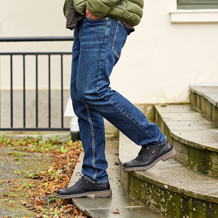 Mann iført blå jeans og svarte sko går ned en utendørs trapp med mose på sidene.