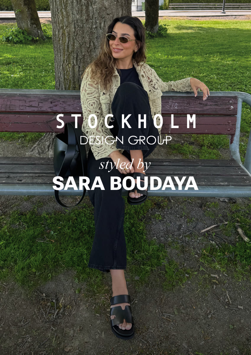 Person på parkbenk med svarte plattformsandaler fra Stockholm Design Group, kremfarget strikkejakke og mørke klær. 
