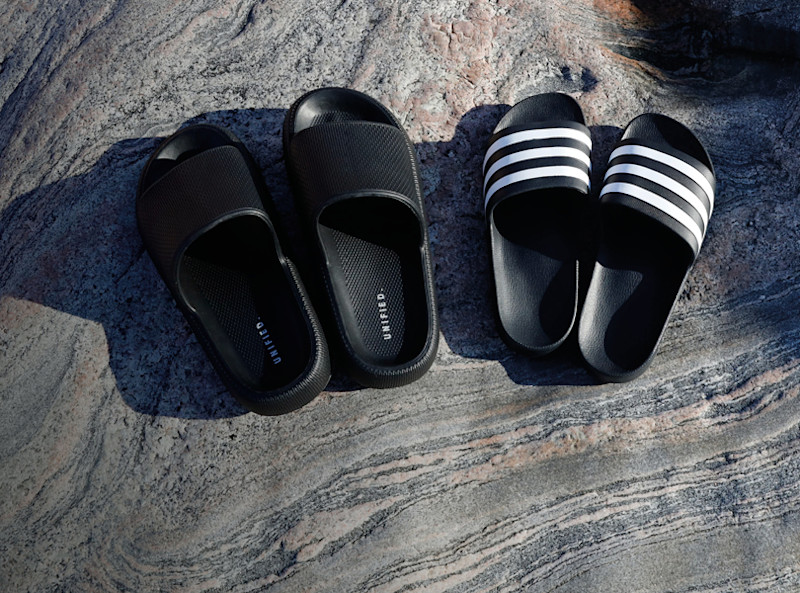 To par svarte slippers på stein: ett helsvart par og ett med hvite striper. Begge er enkle, flate badesandaler.