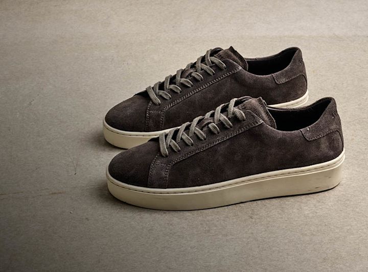 Mørke grå semsket sneakers med hvit såle og snørebånd, lavt skaft og minimalistisk stil.