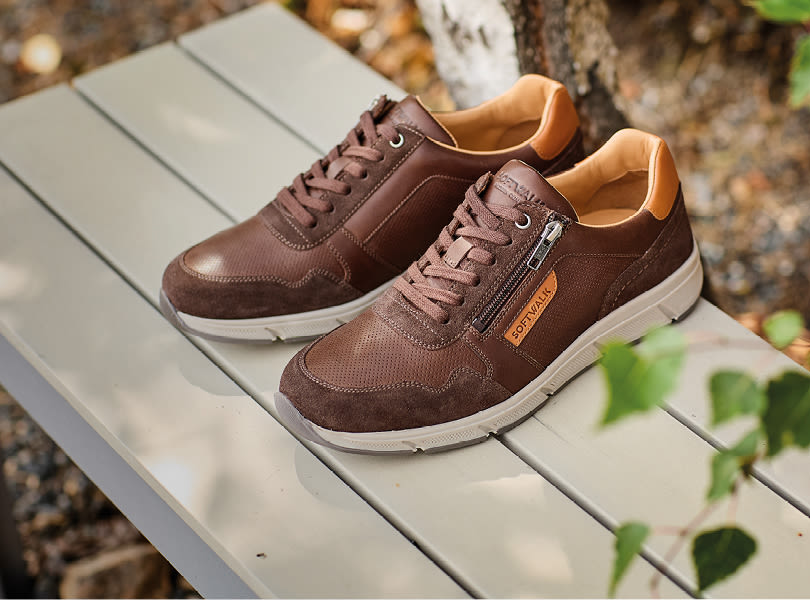 Brune fritidssko fra Softwalk med glidelås og oransje detaljer, plassert på en trebenk utendørs.