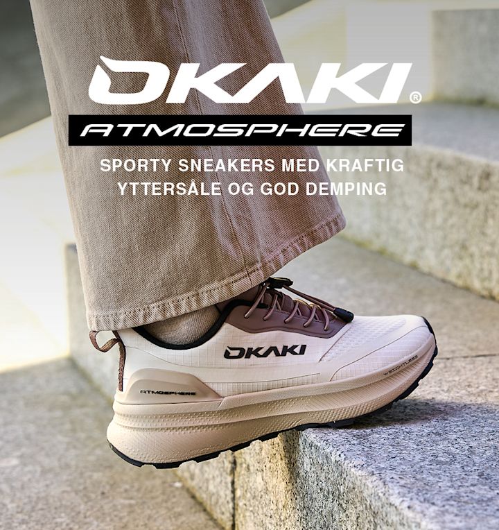 Hvite OKAKI Atmosphere sportssko med brun detalj, vist på person med brune bukser. Tekst fremhever kraftig yttersåle og god demping.