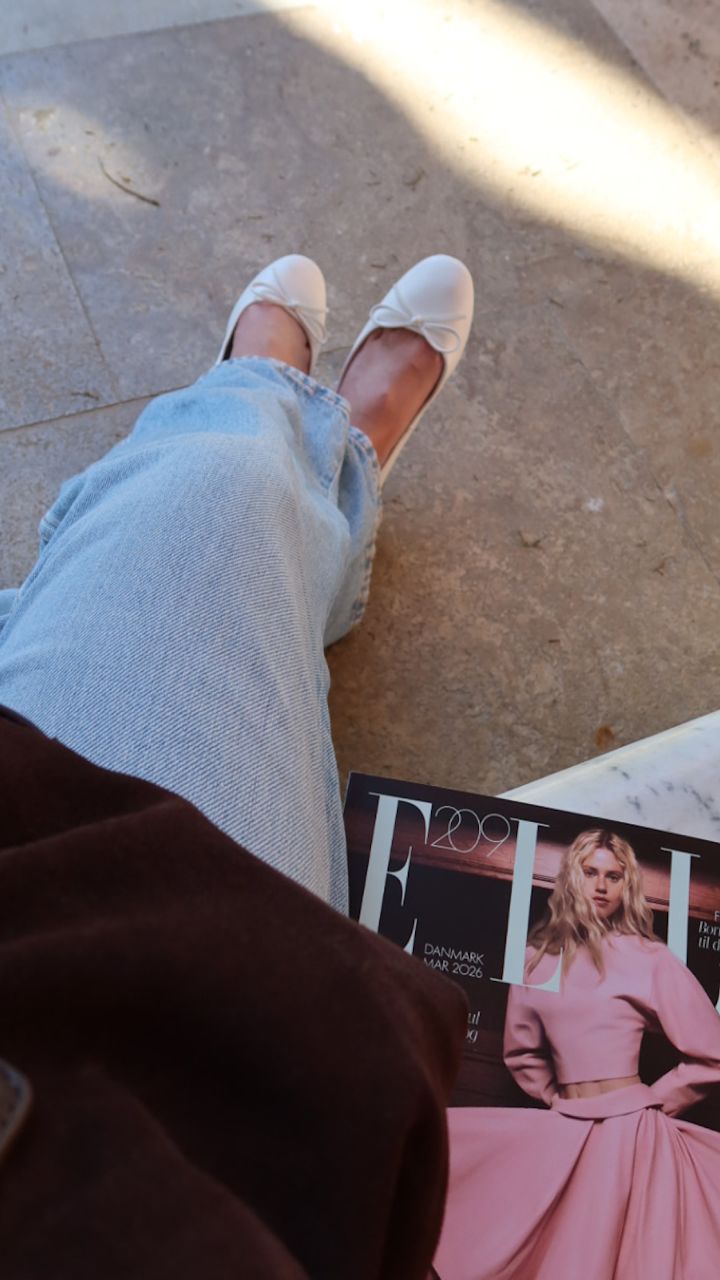 Hvite ballerinasko med sløyfedetalj fra Privé, lyseblå jeans og et ELLE-magasin på steinfliser i sollys.