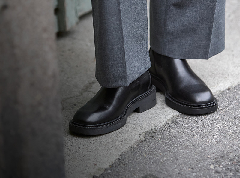 Svarte Chelsea-boots i skinn med tykk såle, stylet med grå bukser. Minimalistisk og elegant design.