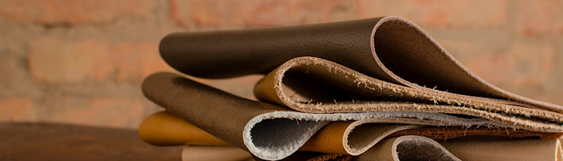 Flere lag med sammenrullet lær i ulike brune nyanser ligger stablet på et bord med en murvegg i bakgrunnen.