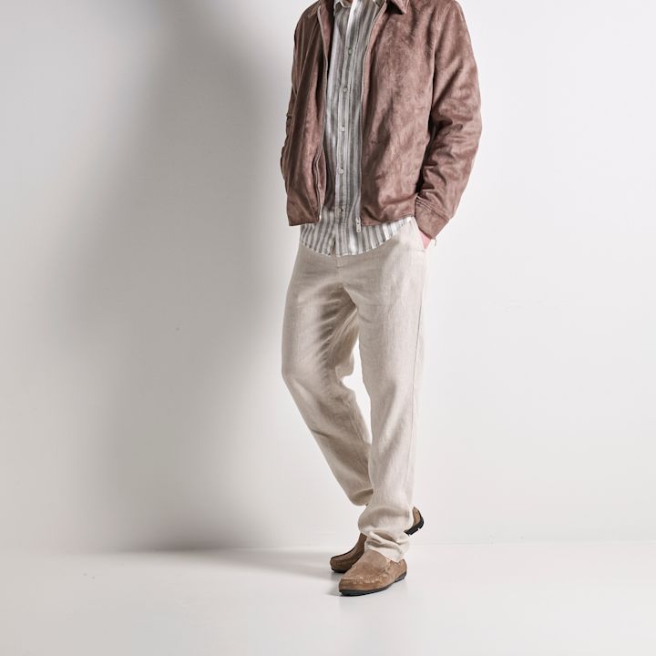 Person i brun mockajacka, randig skjorta och beiga byxor med ljusbruna mockaskor i casual stil.