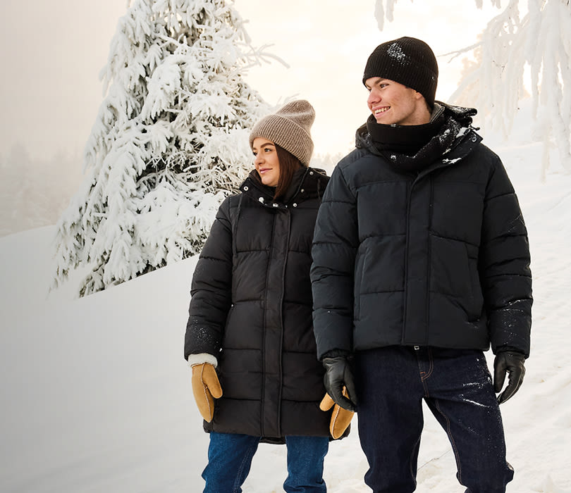 Par i svarte vinterjakker og luer går i snøen, begge med brune vinterstøvler med snøring i robust stil for vinterføre.