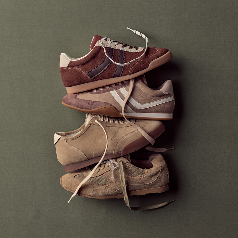 Fire par retro sneakers i brune og beige nyanser med semsket skinn og gummisåler, stablet på en mørkegrønn bakgrunn.