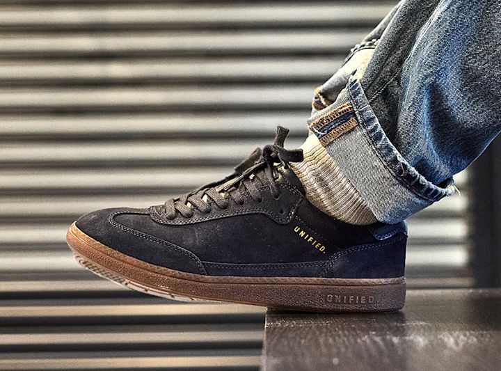 Mörkblå mocka sneakers från Unified med brun gummisula, burna med uppvikta jeans och vita strumpor.