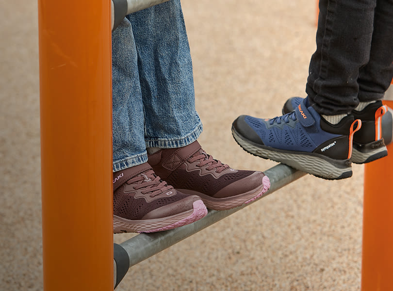 To personer med sportssko på en stang; burgunderrøde joggesko med rosa såle og blå joggesko fra Okaki med oransje detaljer.