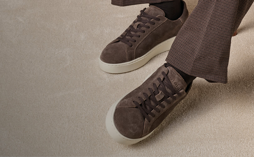 Brune semsket skinnsko fra Stockholm Design Group med hvit såle, brukt med rutete bukser på beige teppe, moderne casual stil.