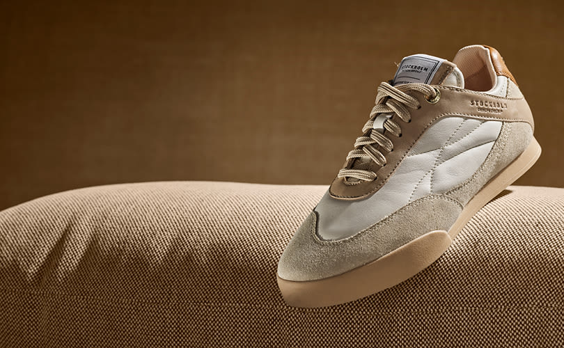 Beige og hvit sneaker i skinn fra Stockholm Design Group, med retro sportslig design, plassert på en beige tekstiloverflate.