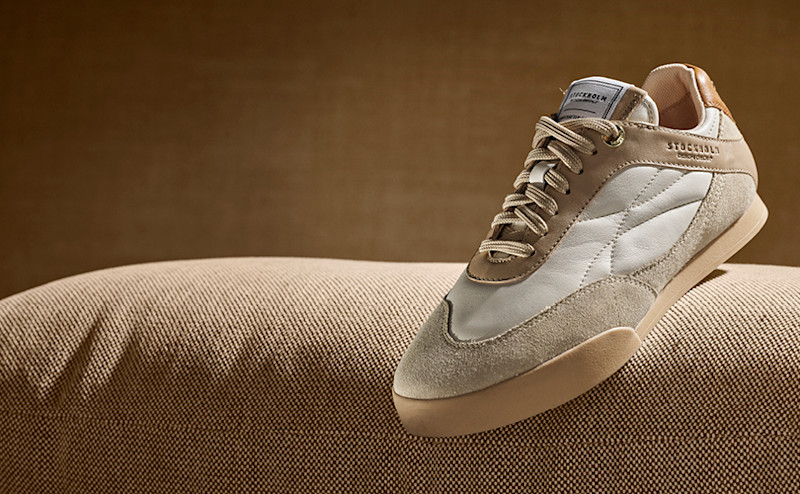 Beige og hvit sneaker i skinn fra Stockholm Design Group, med retro sportslig design, plassert på en beige tekstiloverflate.