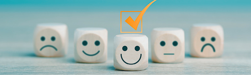 Tre tärningar med ansikten som visar ledsen, neutral och glad, där den glada tärningen i mitten är markerad med en orange bock.