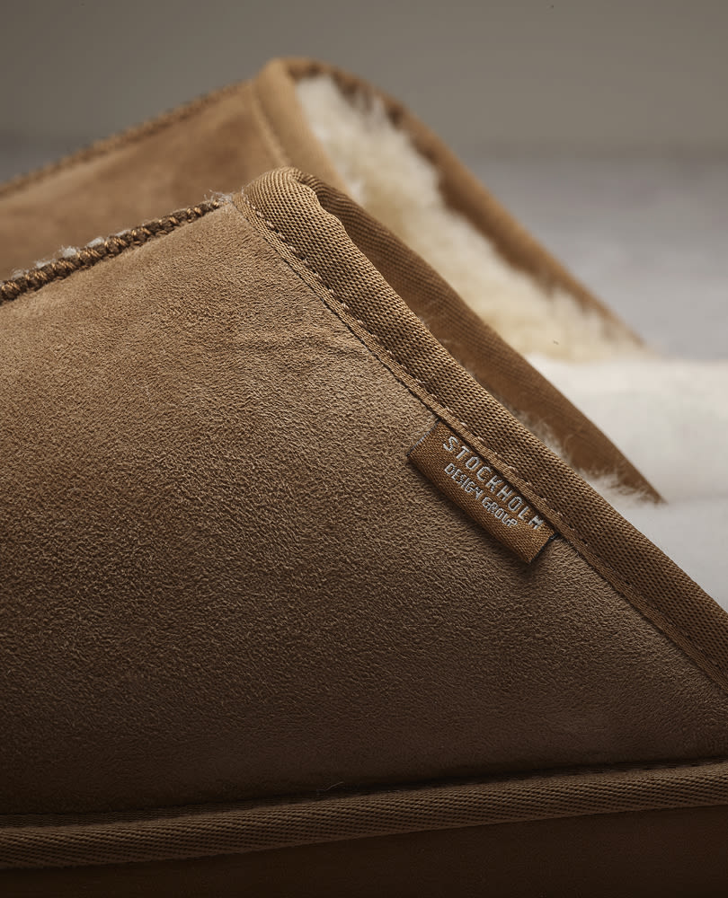 Nærbilde av en brun semsket tøffel med hvit pelsfôr.