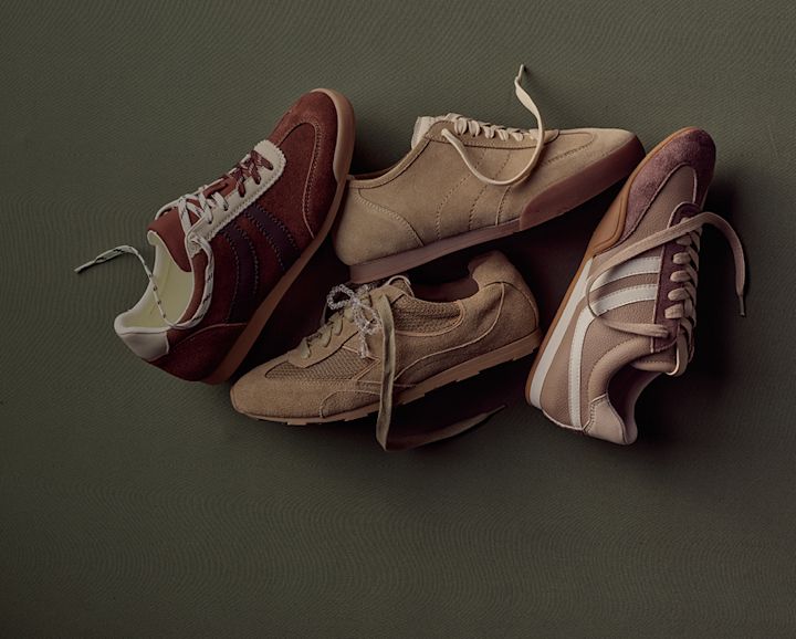 Fire par low profile sneakers i jordfarger - burgunder, beige og brune - arrangert på en mørk grønn bakgrunn.