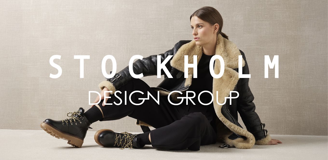Person i skinnjakke med pelskrage og svarte fjellstøvler med gul snøring og gummisåle, Stockholm Design Group-logo.