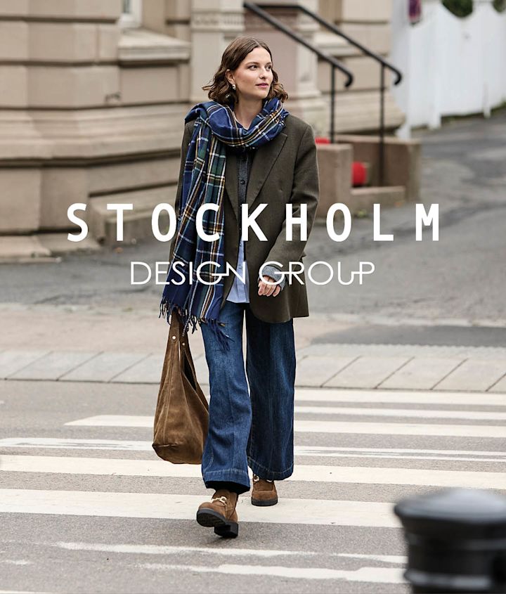 Kvinna går på övergångsställe i bruna chunky boots, jeans, grön kavaj och rutig halsduk.