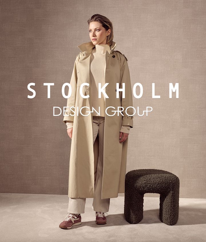 Person i beige trenchcoat med burgunderrøde sneakers fra Stockholm Design Group med beige detaljer. Stockholm Design Group-logo vises i forgrunnen.
