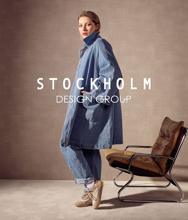 Person i denimkappa och jeans bär beige sneakers från Stockholm Design Group i retrostil. Stockholm Design Group-logotyp syns i förgrunden.