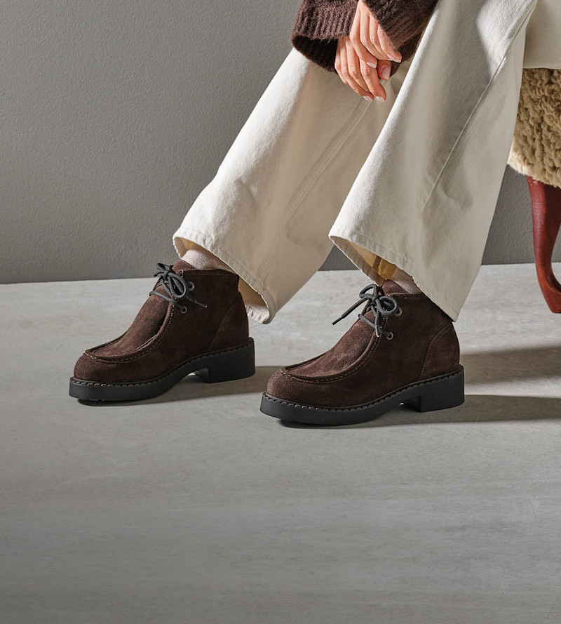 Mörkbruna mockaboots med snörning och tjock svart sula, i casual stil. Bärs med vita vida byxor och brun stickad tröja.