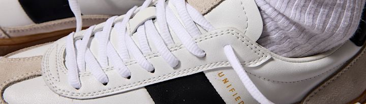 Vita och beige skinnskor med vita snören och svart detalj, bärs med vita ribbstickade strumpor.