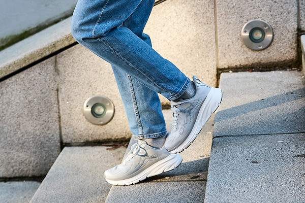 Person i blå jeans går ned betongtrapper med lysegrå Okaki Hyper i sporty stil med hvite såler.