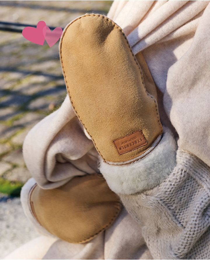 Sandfärgade handskar med vit pälskant från Stockholm Design Group, visas med rosa hjärtsymboler och stickad vit tröja.