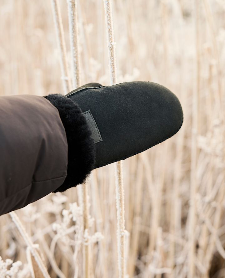 Svart vintervott med myk pelskant som holder en frostdekket plante i et vinterlandskap.