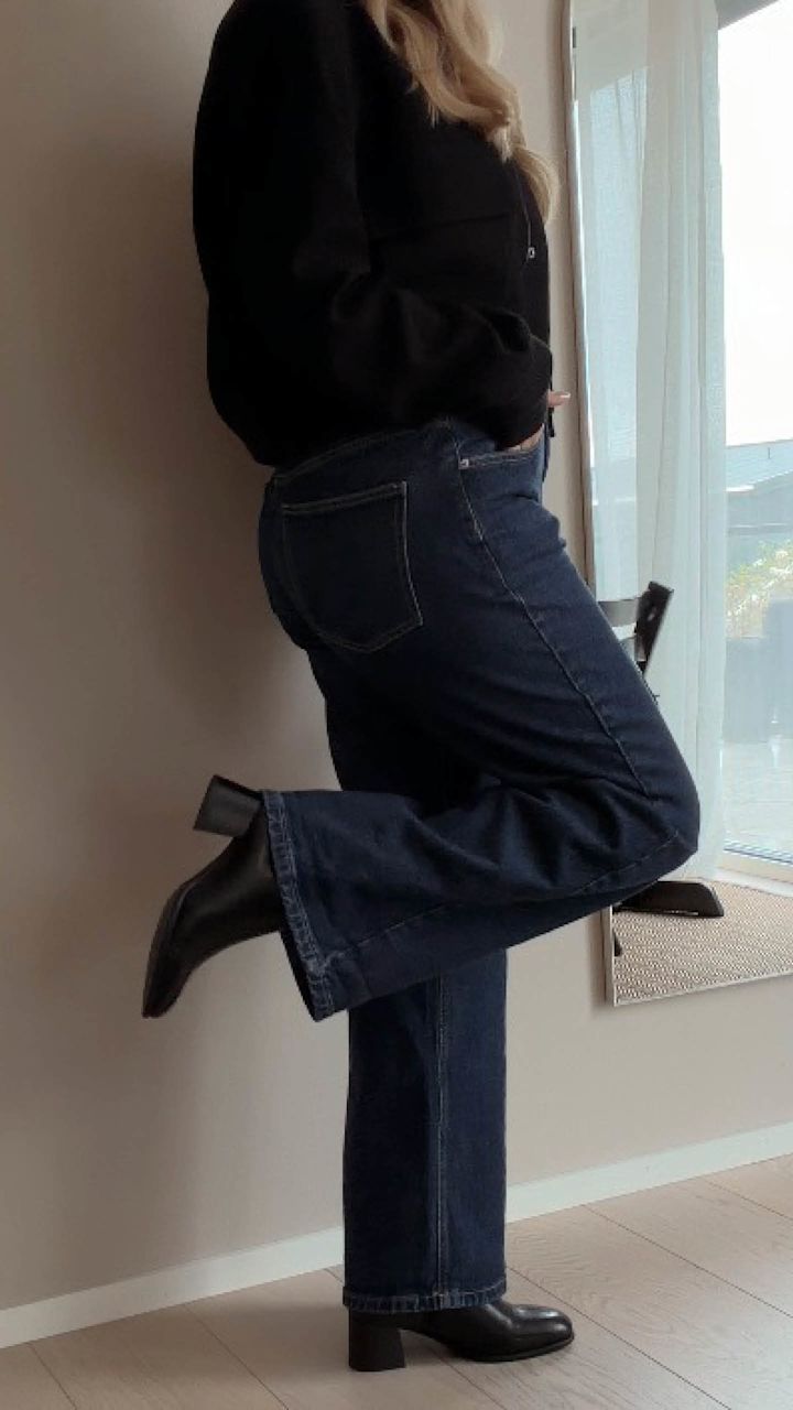 Kvinna i mörkblå wide-leg jeans och svarta läderboots med klack, sedd från sidan.