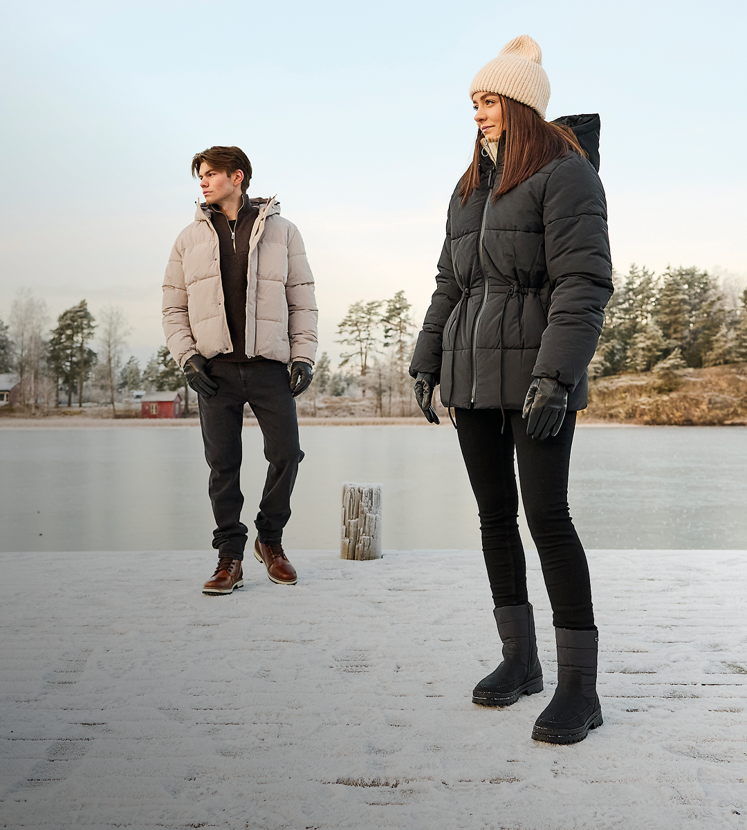 To personer i vinterlandskap ved frossen innsjø, kvinne med svarte vinterstøvler og mann med brune vinterstøvler.