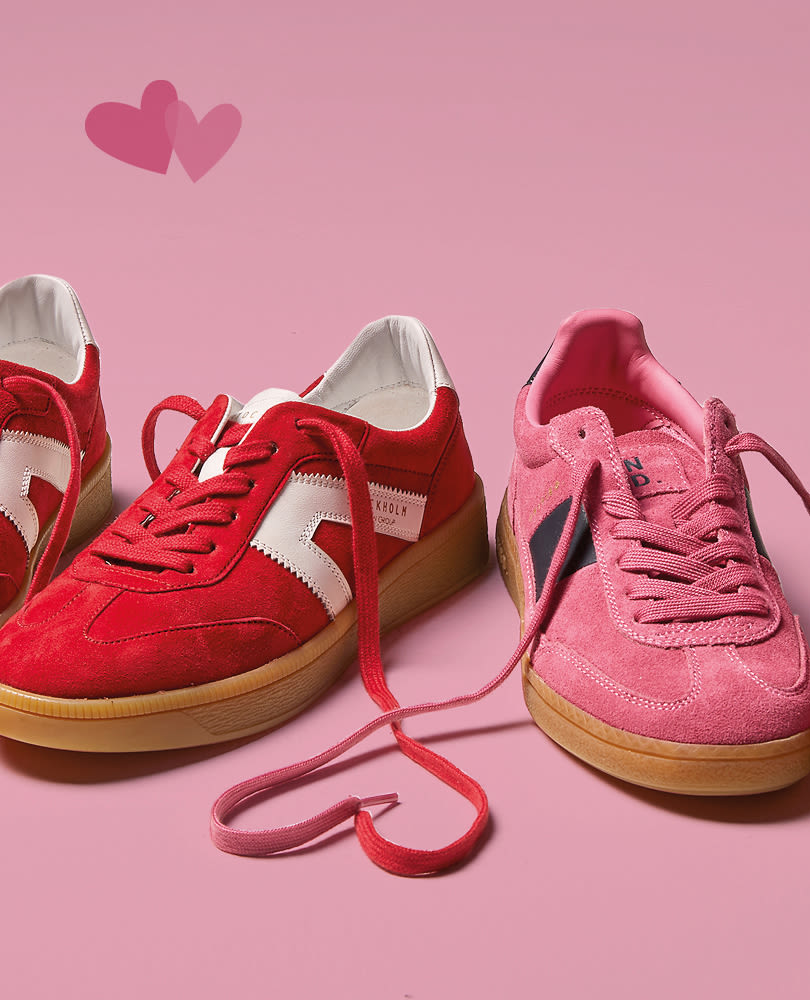 Røde og rosa retro sneakers med gummisula på rosa bakgrunn. Skolissene danner et hjerte, med to hjerter svevende over.