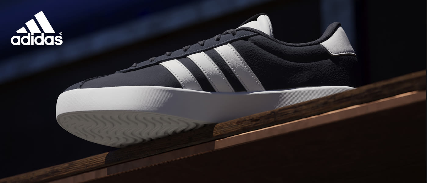 Svart Adidas sneaker med hvite striper og såle, plassert på en treoverflate mot mørk bakgrunn.