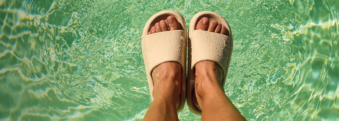 Beige slippers i klart, grønnaktig bassengvann, sett ovenfra i solskinn.