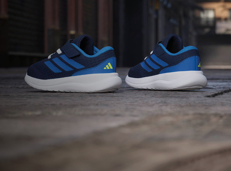 Adidas barnesneakers i marineblå og blå med neongrønt logo, hvit sål og borrelåsrem, sett bakfra.