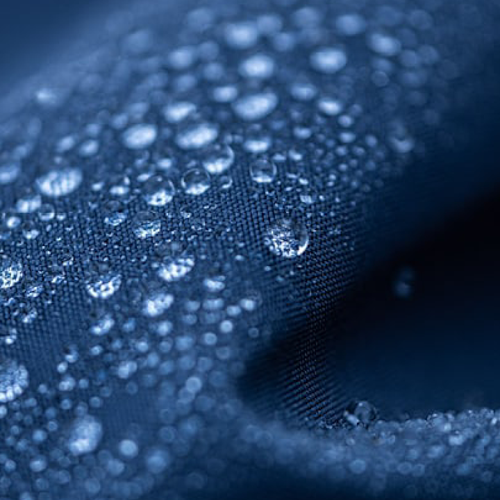 Vattendroppar ligger på ytan av ett mörkblått, vattenavvisande tyg i närbild.
